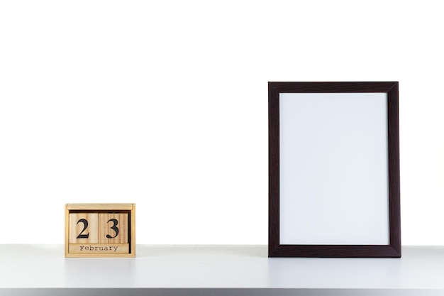 Calendário de madeira 23 de fevereiro com moldura para foto em mesa branca e closeup de fundo