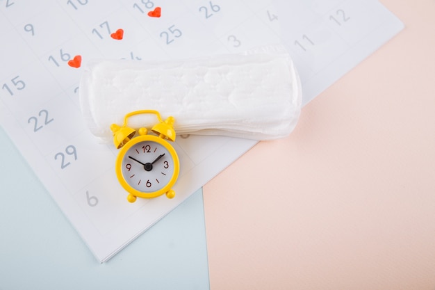 Calendário de menstruação com alarme amarelo e almofadas diárias em fundo rosa. Dias críticos de mulher, conceito de proteção de higiene de mulher.