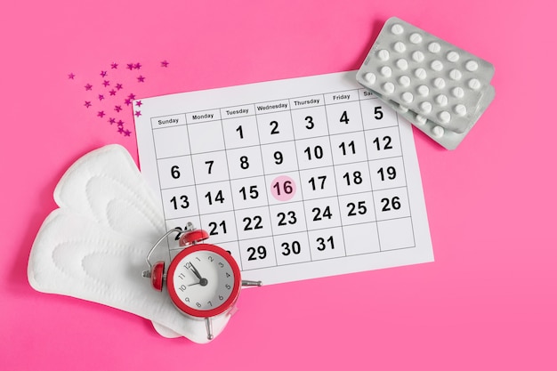 Calendário de menstruação com almofadas, despertador, pílulas anticoncepcionais hormonais. Conceito de ciclo menstrual da fêmea. Analgésicos para dor menstrual