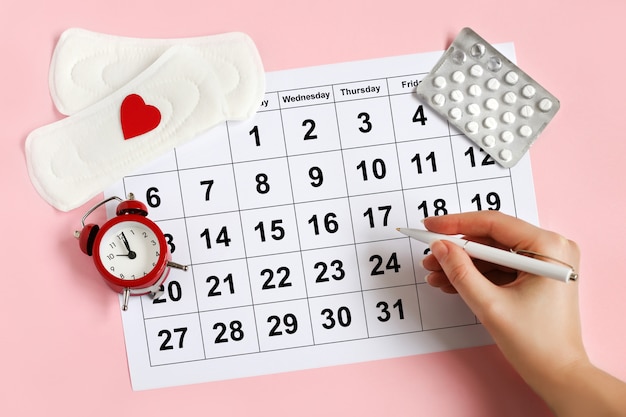 Calendário de menstruação com almofadas, despertador, pílulas anticoncepcionais hormonais. Conceito de ciclo menstrual da fêmea.