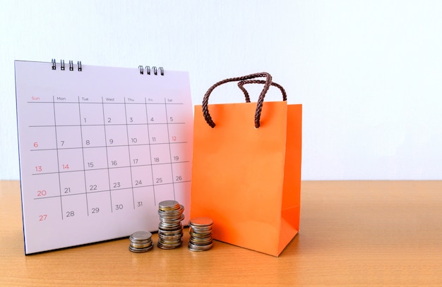 Calendario con días y bolsa de papel naranja en mesa de madera. concepto de compra