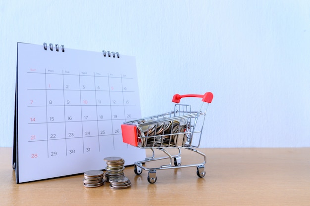 Foto calendario con días y carro supermercado en mesa de madera. concepto de compra