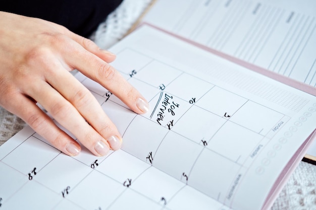 Calendário do planejador com texto Entrevista de emprego na data Mãos femininas escrevendo Data da entrevista de emprego em um calendário Mulher escreve no calendário impresso com palavras de marca e entrevista de emprego