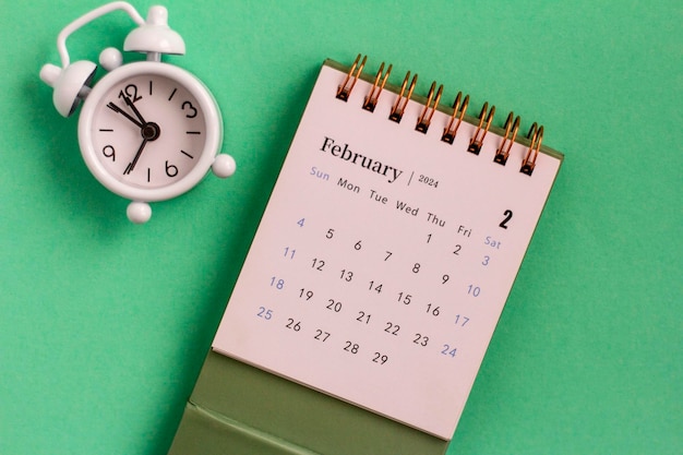 Calendario de escritorio para febrero y reloj sobre un fondo verde