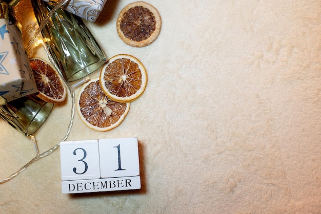 Foto calendario con la fecha 31 de diciembre sobre un fondo de naranjas vasos de guirnalda sobre un fondo beige decoración navideña