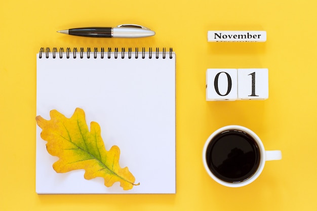 Foto calendario de madera 1 de noviembre taza de café, libreta con bolígrafo y hoja amarilla sobre fondo amarillo