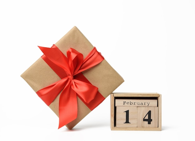 Calendario de madera con fecha 14 de febrero y caja con un regalo sobre fondo blanco, día de san valentín