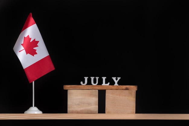Calendario de madera de julio con bandera canadiense sobre fondo negro Vacaciones de verano en Canadá