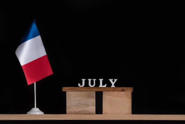 Calendario de madera de julio con bandera francesa sobre fondo negro. Vacaciones de Francia en julio.