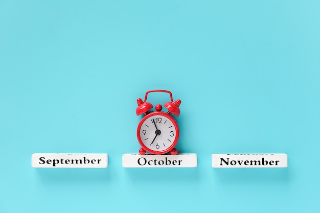 Calendario de madera meses de otoño y despertador rojo en octubre