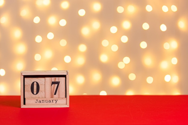 calendario de madera de navidad el 7 de enero sobre fondo rojo y fondo de luces de cerca