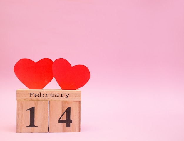 Calendario de madera sobre un fondo rosa con corazones rojos. San Valentín 14 de febrero