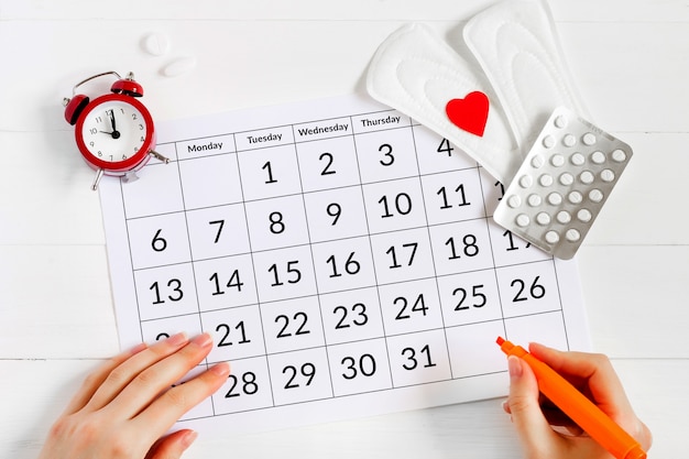 Calendario de la menstruación con almohadillas, reloj despertador, píldoras anticonceptivas hormonales. Concepto de ciclo menstrual femenino. Calmante para el dolor menstrual