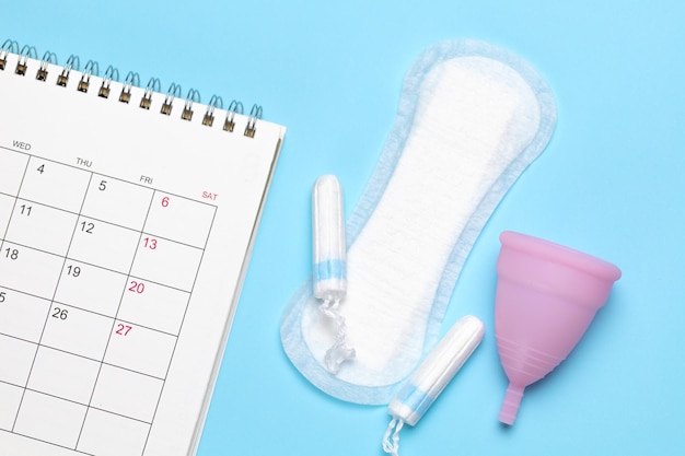 Foto calendario de menstruación calendario con almohadillas y tampones sobre un fondo azul.