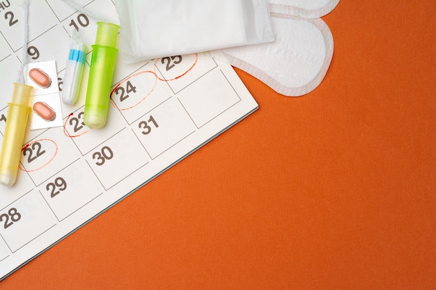 Calendario de menstruación con toallas sanitarias y tampones, vista superior de pastillas