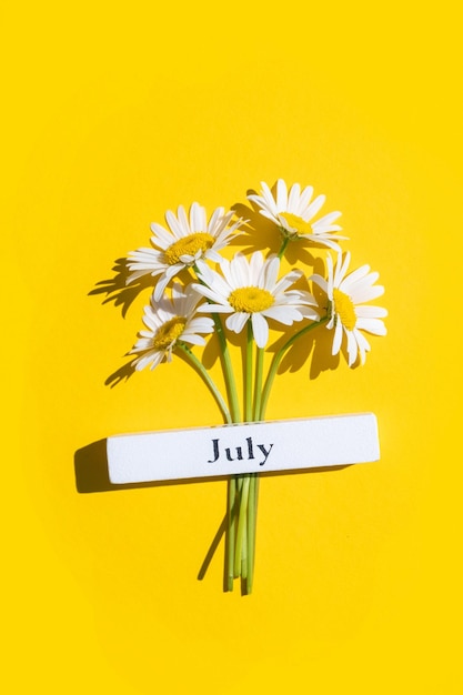 Calendário mês de verão julho e flores de camomila em fundo amarelo vista superior flat lay conceito mínimo olá junho vista superior cartão de saudação plano lay