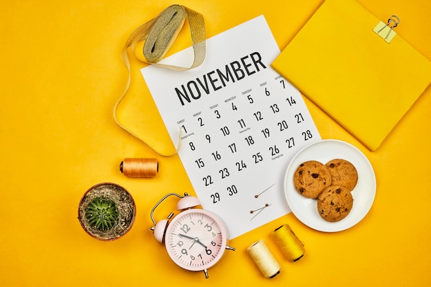 Calendario de noviembre en el escritorio de color amarillo brillante. El espacio de trabajo brillante de una modista o diseñadora de moda