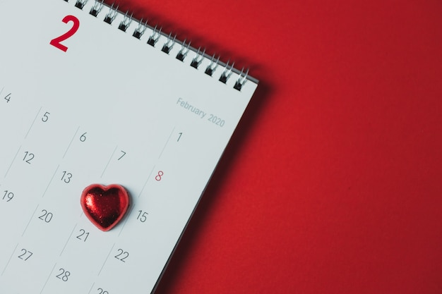 Foto calendario de papel blanco colocado sobre una mesa roja, vista superior y espacio de copia, tema del día de san valentín