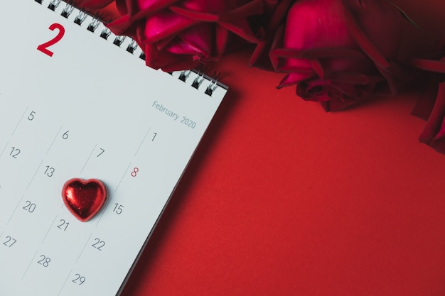 Foto calendario de papel blanco y rosa roja colocada sobre una mesa roja, vista superior y espacio de copia, tema del día de san valentín