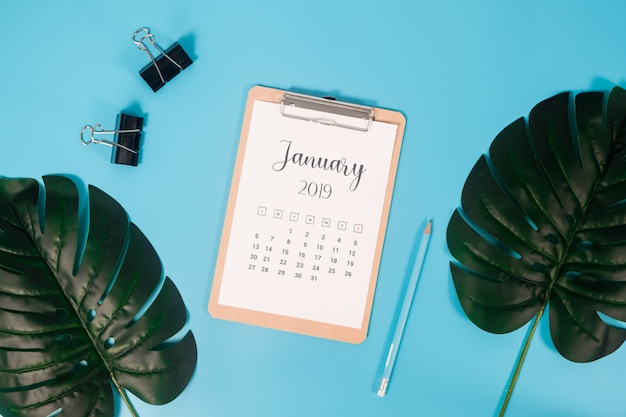 Calendario plano de la endecha con el tablero, las hojas de palma y el lápiz en fondo azul.