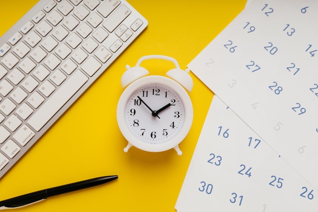 Calendario de teclado blanco y despertador sobre fondo amarillo Fecha límite y concepto de tareas urgentes