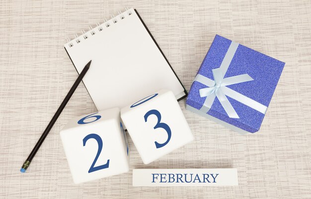 Calendario con texto y números azules de moda para el 23 de febrero y un regalo en una caja.