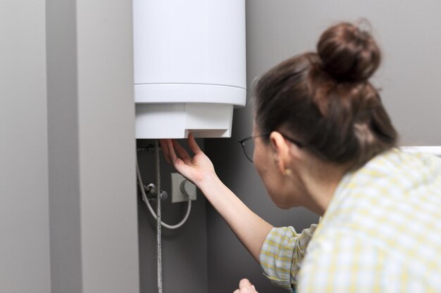 Calentador de agua doméstico, una mujer regula la temperatura en un calentador de agua eléctrico, comodidad y agua caliente en la casa