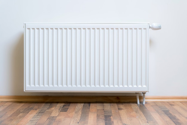 Foto calentador de radiador casero en la pared blanca sobre piso de madera. equipo de calentamiento ajustable para apartamento y hogar.