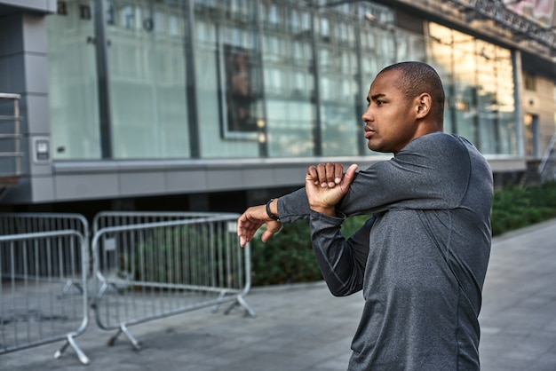 Calentamiento antes de entrenar cerca de atlético hombre africano estirando sus brazos antes de cardio