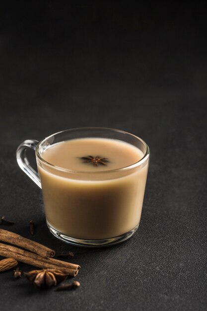 El calentamiento popular de Asia bebe té de masala en una taza de vidrio transparente con cilantro, canela y tallo de rosa sobre un fondo negro.