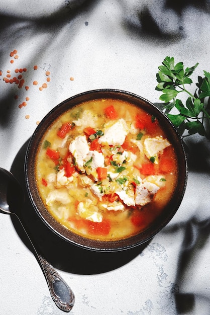 Calentamiento de sopa de otoño con lentejas rojas filete de pollo verduras especias y paprika comida reconfortante Mesa blanca luz dura con sombras de hojas vista superior