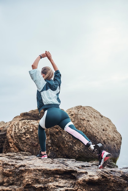 Calentamiento vista posterior de la mujer deportista discapacitado deportivo en ropa deportiva con pie de prótesis de pierna