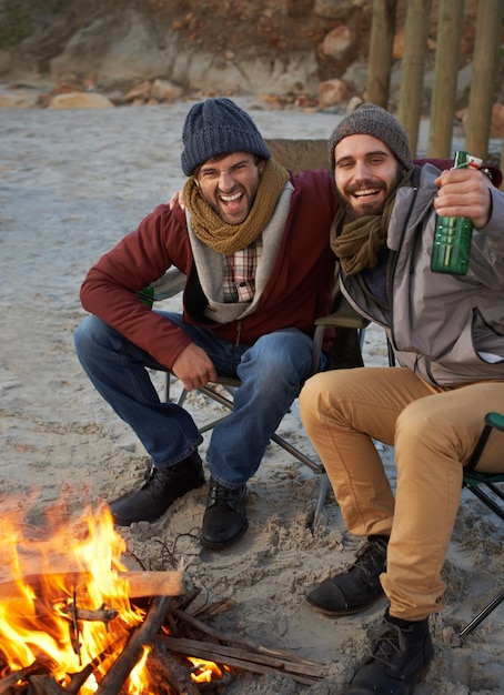 Calentando fuego y cerveza Dos jóvenes sentados alrededor de una fogata en la playa