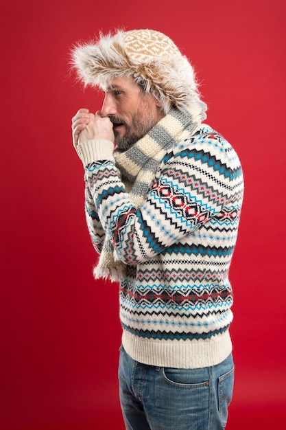 Calentando. Moda de invierno. Complementos tejidos. Condiciones frías del invierno. Hombre guapo con barba con fondo rojo de sombrero y bufanda. Piel sintética. Concepto de moda masculina. Coleccion de moda. Ropa de moda.