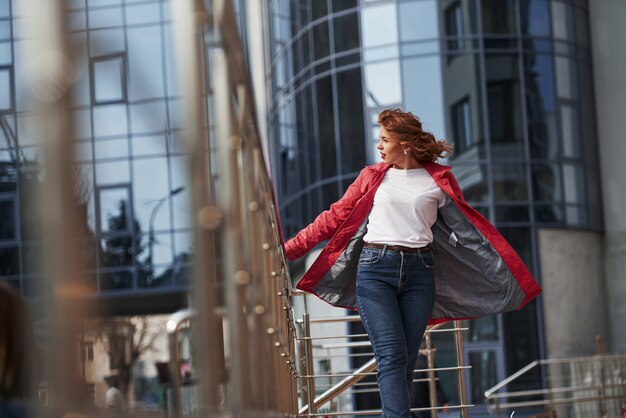 Calentando un poco. Mujer bonita adulta en abrigo rojo cálido tiene caminar en la ciudad en su tiempo de los fines de semana