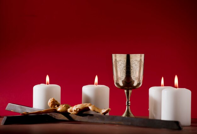 Foto cálice cristão com crucifixo e velas acesas na mesa marrom fundo vermelho