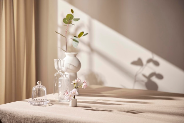 La cálida luz del sol que entra por la ventana con fondo beige flores jarrones y una mesa