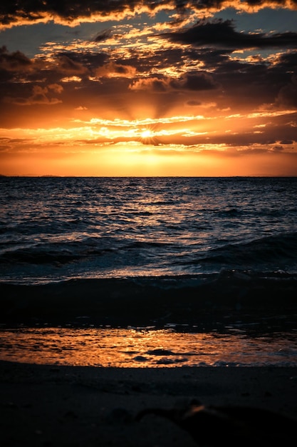 Foto cálida puesta de sol vista desde una playa con olas y nubes
