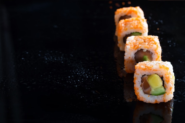 California Maki Sushi Roll hecho de carne de cangrejo, aguacate, pepino sobre fondo de vidrio negro