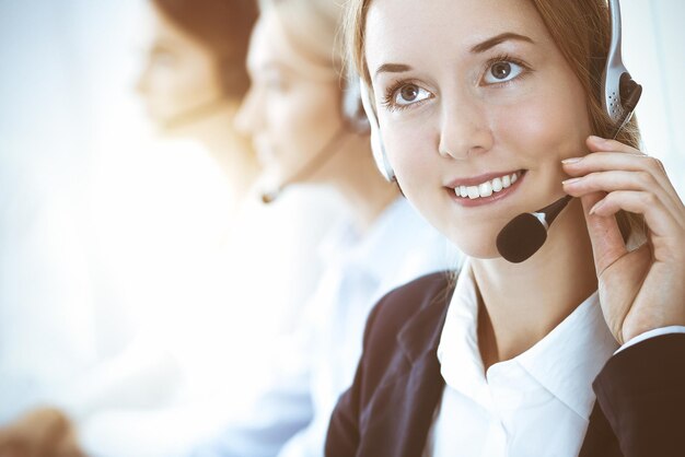 Call center e conceito de pessoas de negócios. Mulher de negócios bonita com clientes de consultoria de fones de ouvido. Grupo de diversos operadores de telefone no trabalho no escritório.