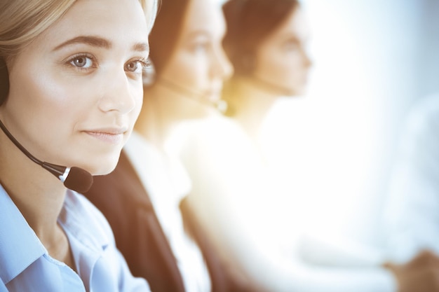 Call center e conceito de pessoas de negócios. Mulher de negócios bonita com clientes de consultoria de fones de ouvido. Grupo de diversos operadores de telefone no trabalho no escritório.