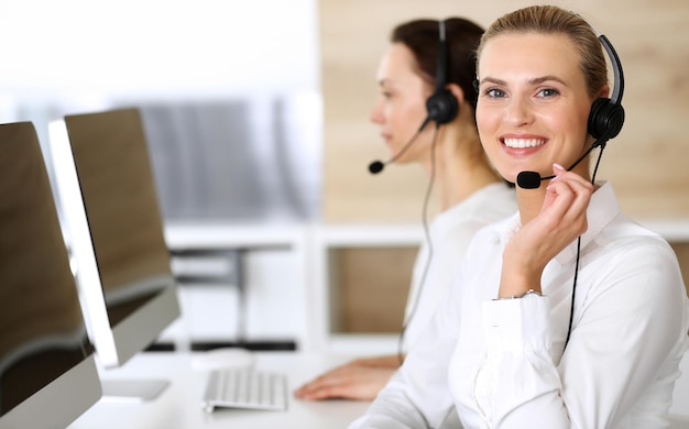 Callcenter Glückliche und aufgeregte Geschäftsfrau, die ein Headset verwendet, während sie Kunden online berät Kundendienstbüro oder Telemarketing-Abteilung Lächelnde Gruppe von Operatoren bei der Arbeit