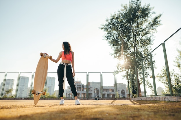 Calle elegante foto de niña en ropa casual de pie con una patineta