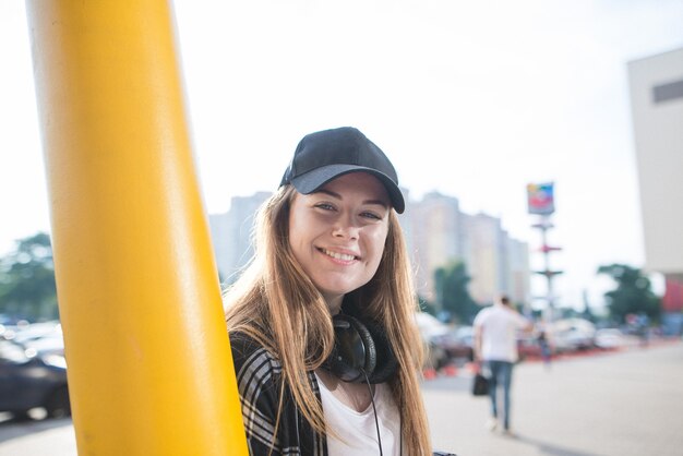 Calle sonriente chica elegante en ropa casual y auriculares en el fondo del paisaje urbano