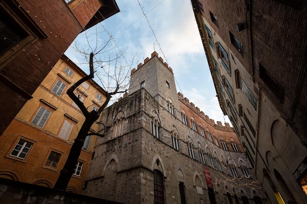 El callejón de edificios antiguos en la ciudad de Siena está decorado con iluminación de Año Nuevo Italia