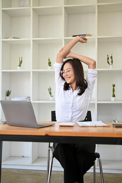 Calma e relaxada empresária asiática esticando os braços em sua mesa