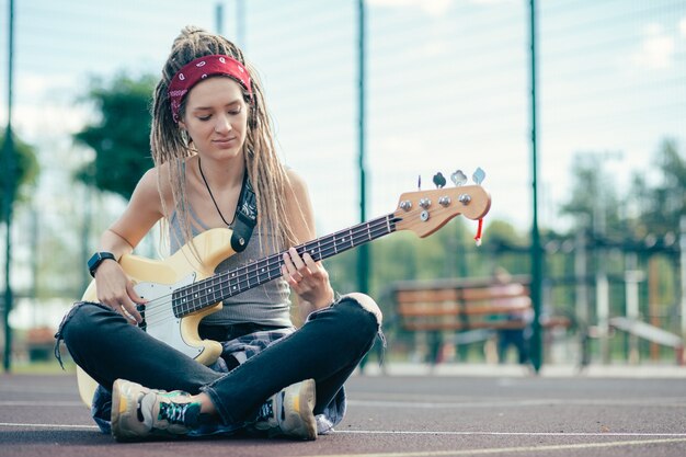 Calma joven pensativo mirando la guitarra mientras la toca en el campo de deportes