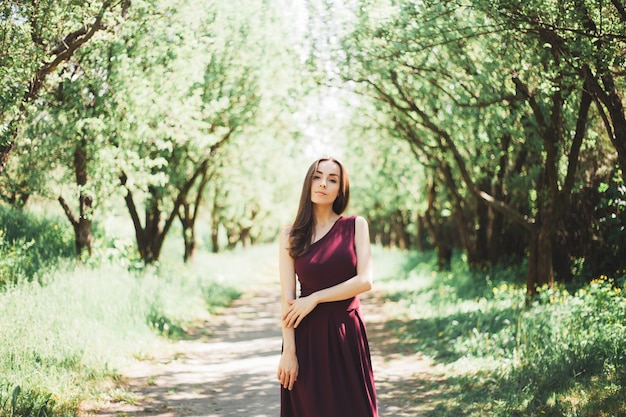 Calma linda jovem morena com um vestido estiloso caminhando e posando no jardim de verão