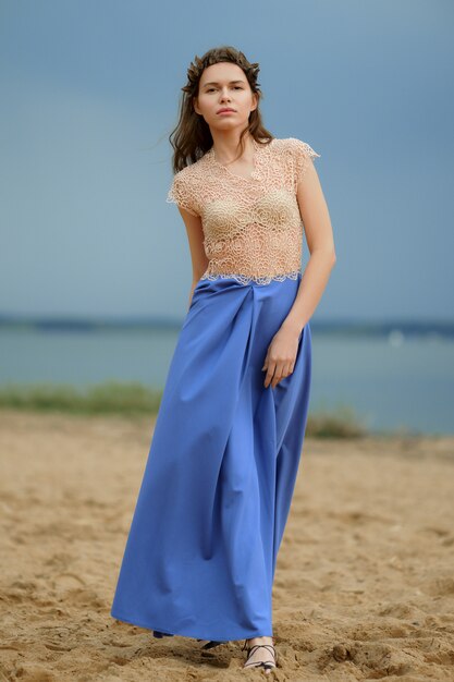Foto calma modelo solitário na praia de saia azul e blusa transparente.