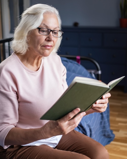 Calma mulher sênior lendo um livro enquanto está sentado na sala de estar